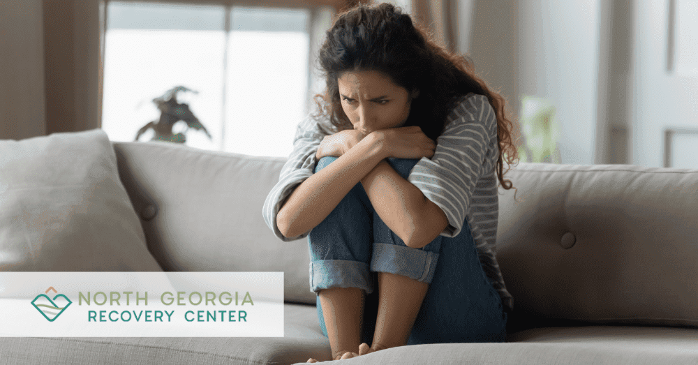 Distraught woman holding knees in a crouched position on the couch