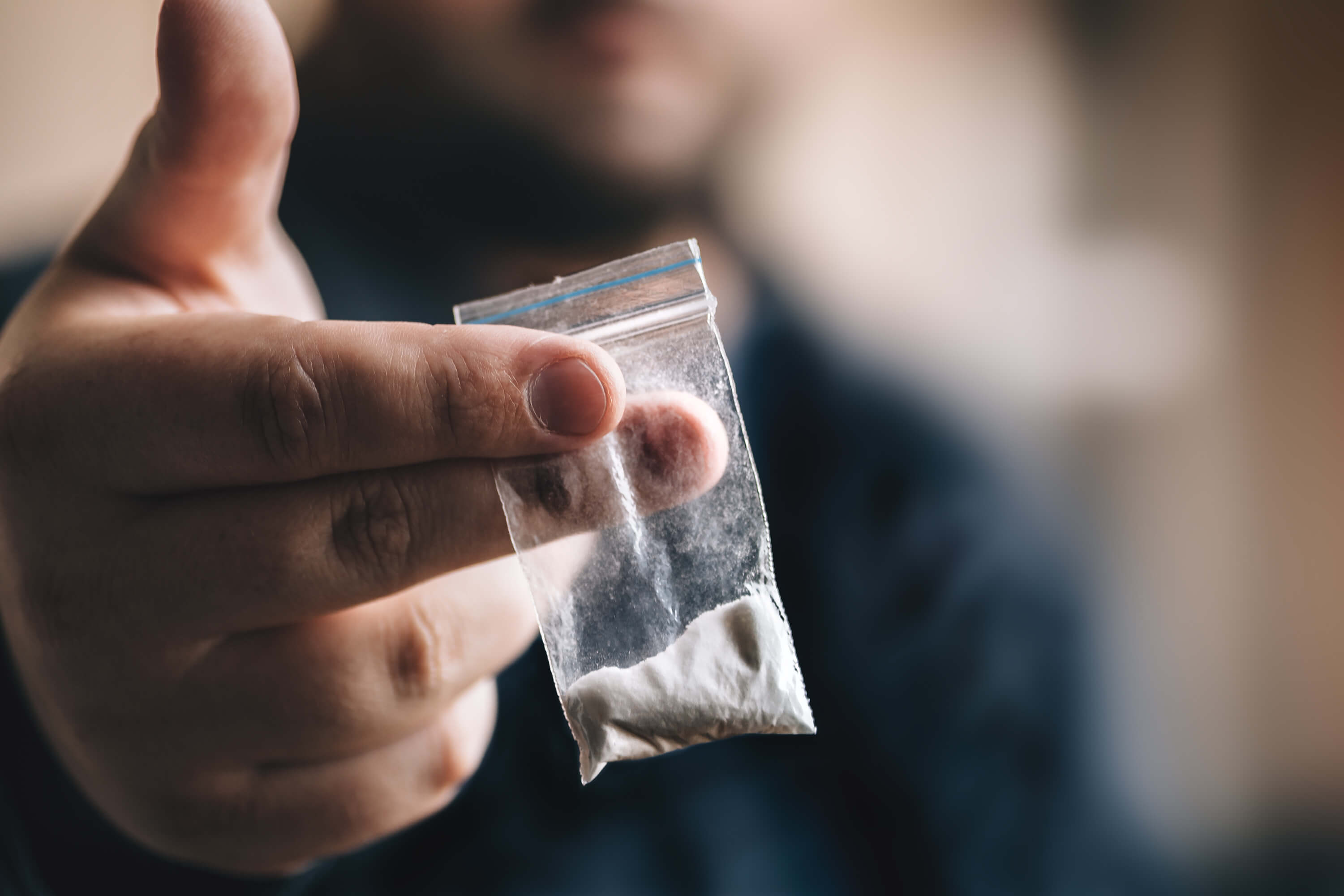 close-up photo of a person holding a small bag of cocaine between their fingers